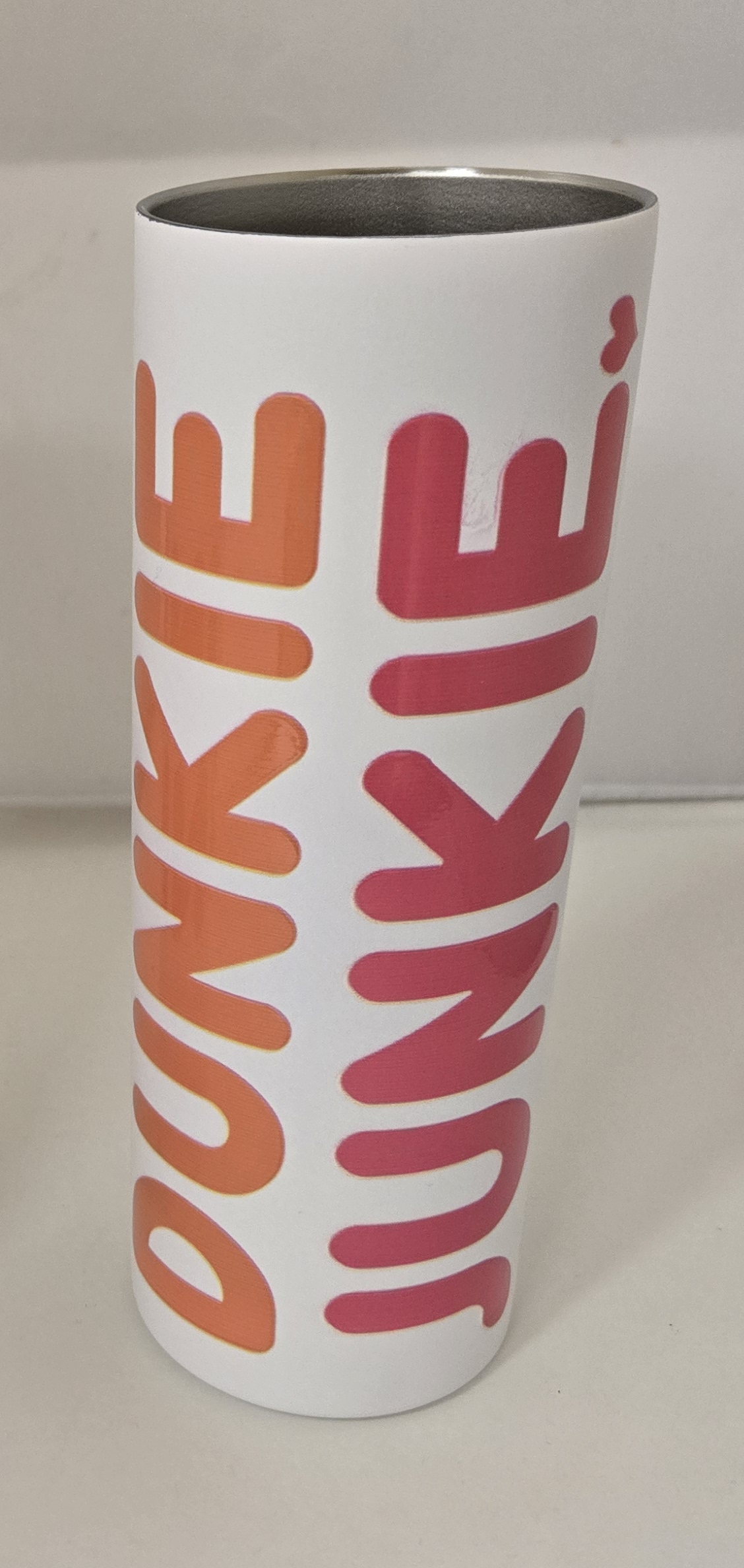 Dunkin Junkie 20oz Skinny Tumbler with bold orange and pink lettering on a white background, designed for stylish and portable drink storage.