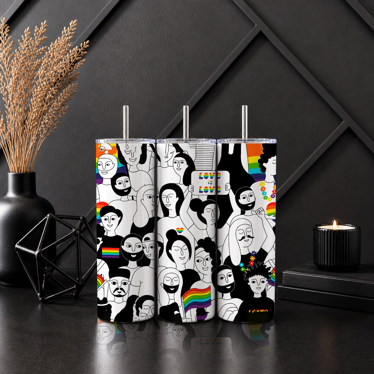 Three stainless steel tumblers with colorful black-and-white illustrations of diverse people and rainbow details on a dark modern table, featuring the Love Is Love Pride Tumbler – LGBTQ Rainbow Inclusive Drinkware.