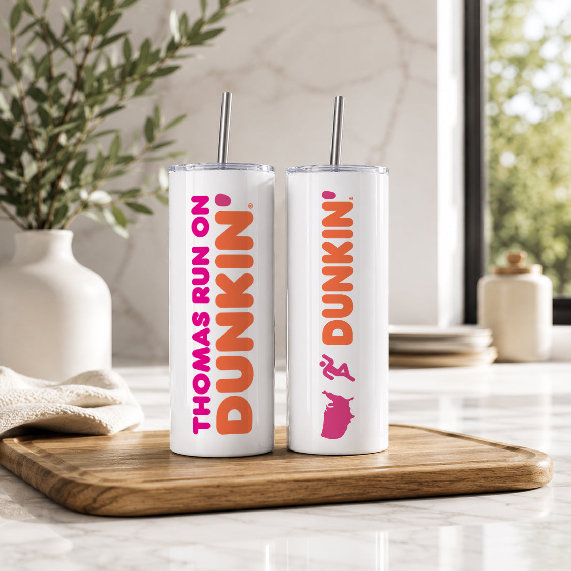 Two white insulated tumblers with metal straws featuring custom Dunkin style designs and text, displayed on a wooden tray in a bright kitchen setting, showcasing the Personalized Name Tumbler – Custom Dunkin Style Insulated Cup with Straw | Custom Name Gift.