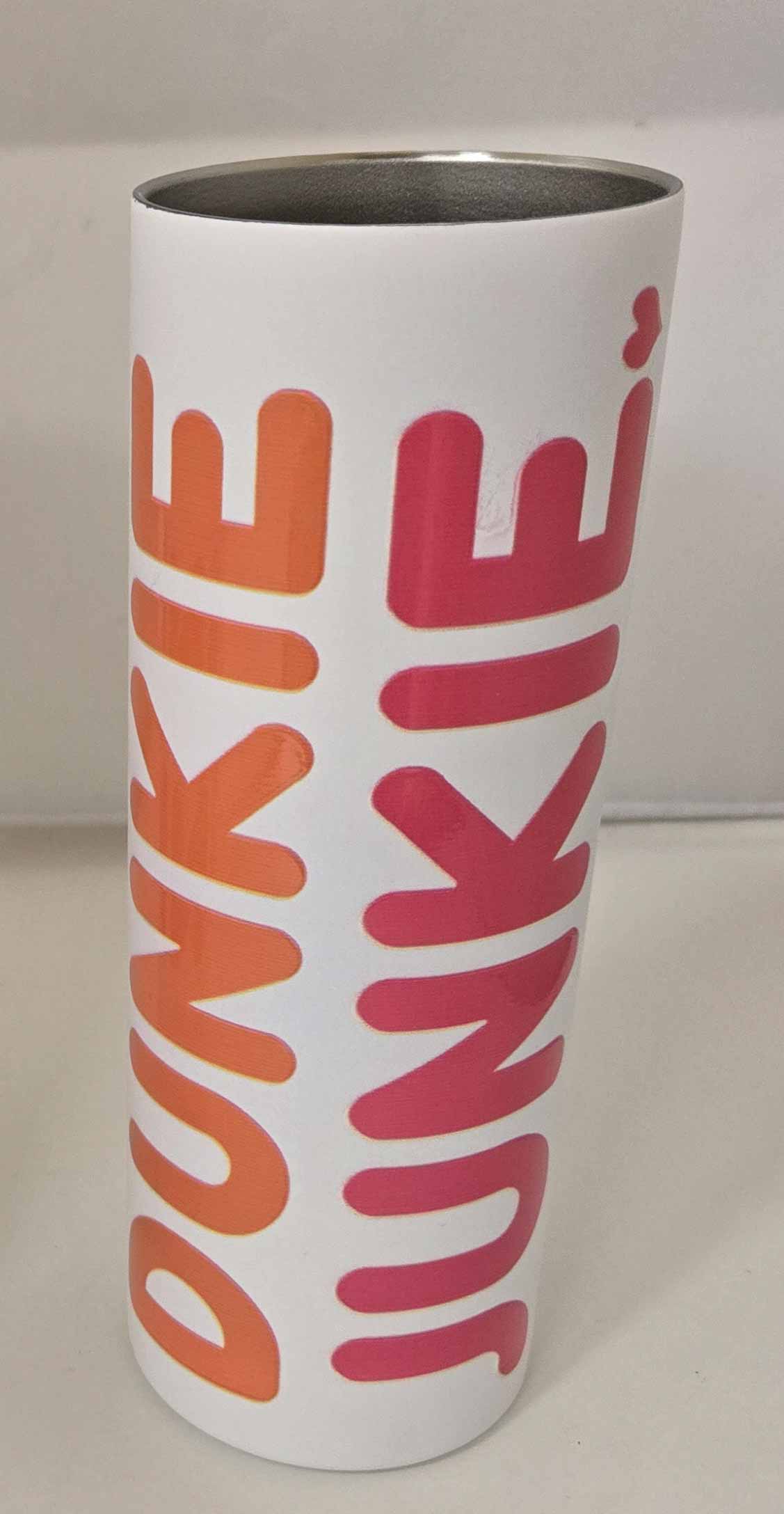 White tumbler with bold orange and pink text reading Dunkin Junkie, featuring a stainless steel interior, called Dunkin Junkie 20oz Skinny Tumbler